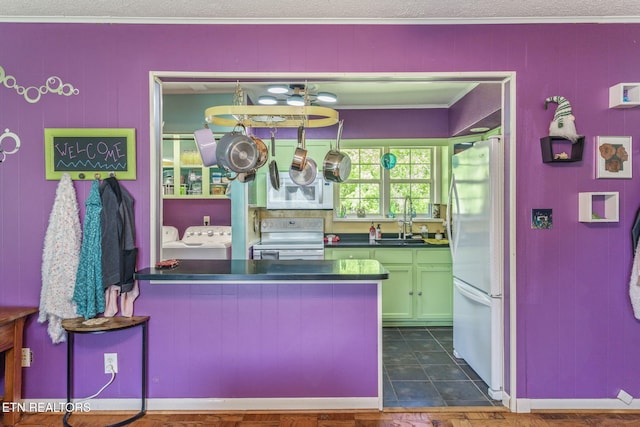 kitchen with washer and dryer, a sink, dark countertops, white appliances, and ornamental molding