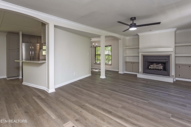 unfurnished living room featuring crown molding, arched walkways, dark wood finished floors, ceiling fan with notable chandelier, and baseboards