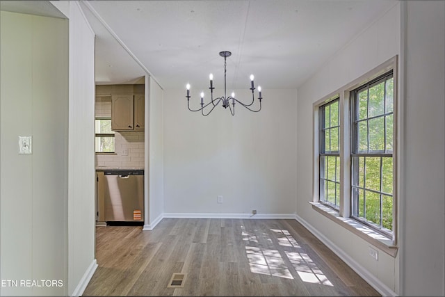 unfurnished dining area with visible vents, baseboards, wood finished floors, and a chandelier