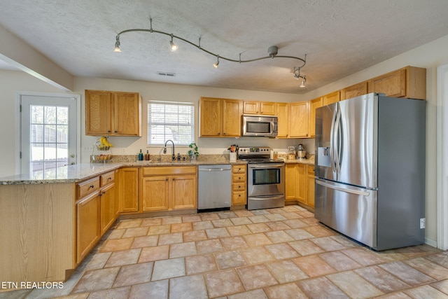 kitchen with a peninsula, a sink, visible vents, appliances with stainless steel finishes, and light stone counters