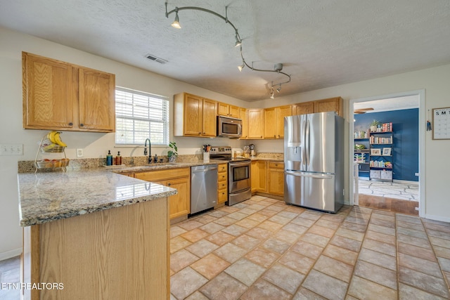 kitchen with a sink, a peninsula, visible vents, light stone countertops, and appliances with stainless steel finishes