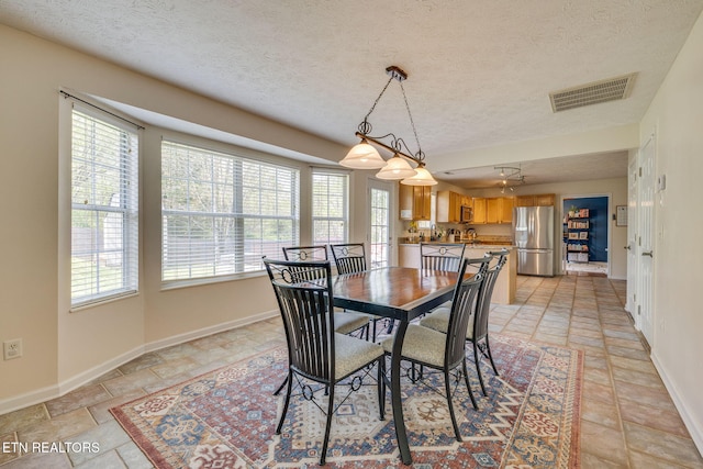 dining room with a textured ceiling, visible vents, baseboards, and stone finish flooring