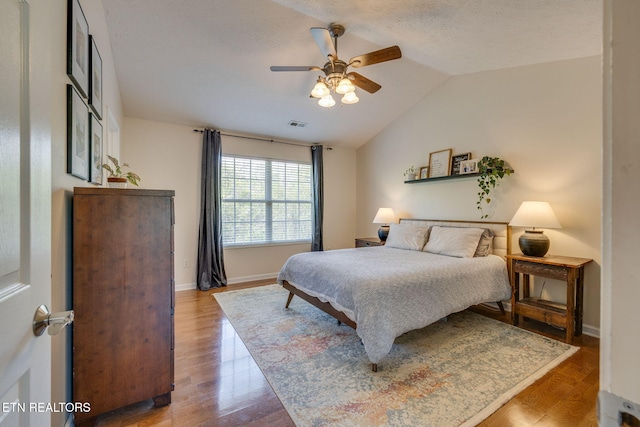 bedroom featuring lofted ceiling, a ceiling fan, baseboards, visible vents, and wood finished floors