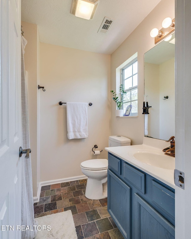 bathroom with toilet, vanity, visible vents, stone finish flooring, and baseboards