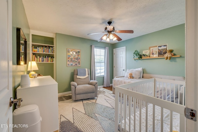 bedroom featuring a textured ceiling, baseboards, ceiling fan, and a crib