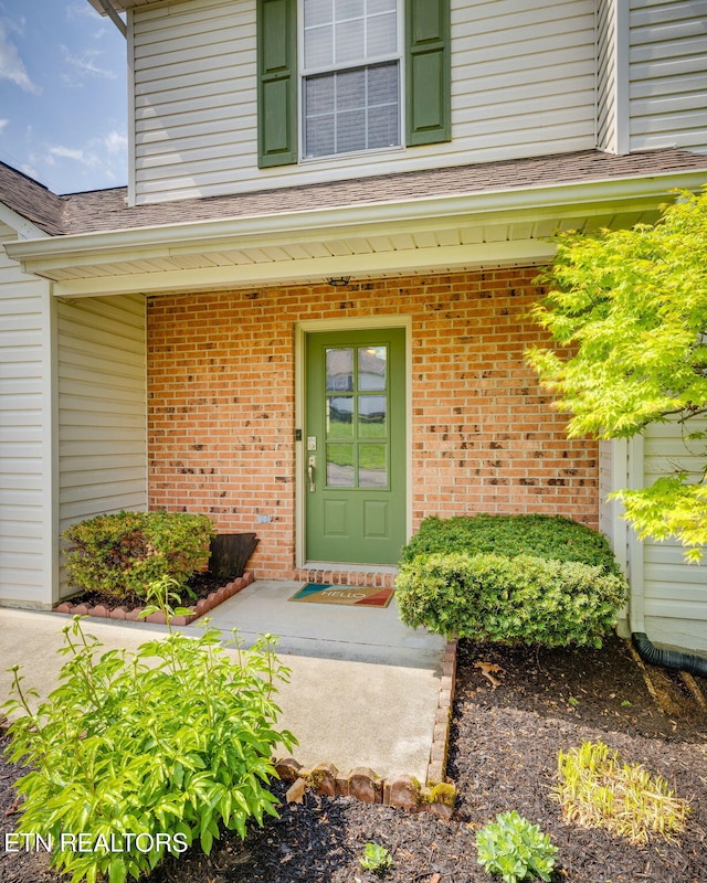 property entrance featuring brick siding and roof with shingles