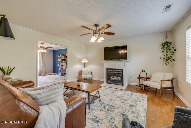 living area featuring a textured ceiling, ceiling fan, visible vents, a fireplace with flush hearth, and wood finished floors