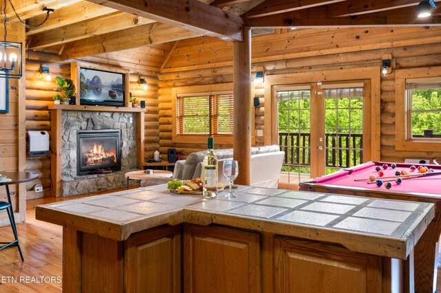 kitchen featuring rustic walls, a stone fireplace, tile counters, light wood-type flooring, and lofted ceiling with beams