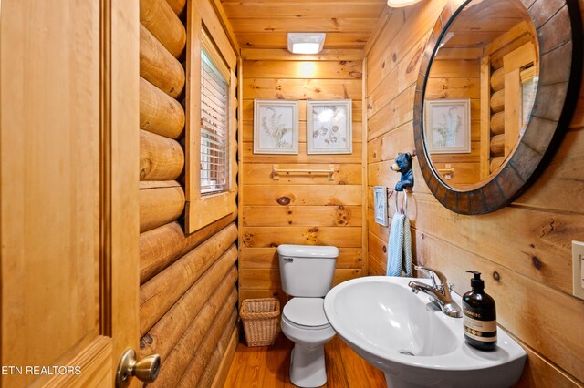half bath with wooden walls, a sink, toilet, wooden ceiling, and wood finished floors