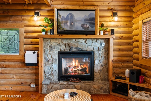 room details with a stone fireplace, log walls, and wood finished floors