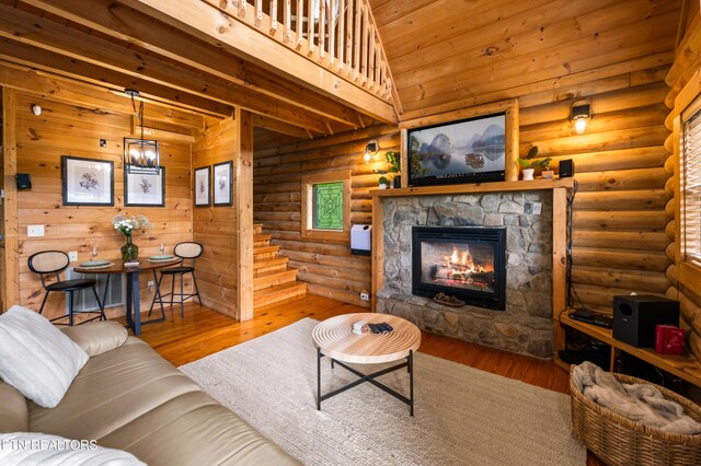 living area featuring a stone fireplace, stairs, wood finished floors, and log walls