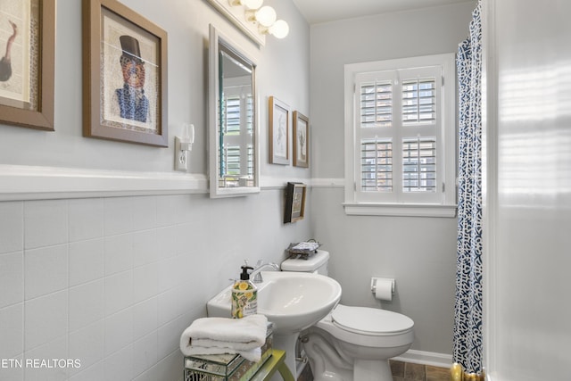 full bathroom featuring toilet, a shower with curtain, tile walls, and wainscoting