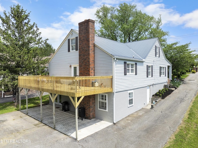 view of home's exterior with a patio, a chimney, metal roof, and a wooden deck