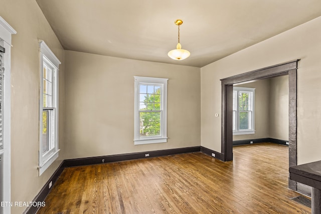 empty room with baseboards, wood finished floors, a healthy amount of sunlight, and visible vents