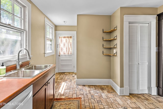 kitchen with baseboards, a sink, brick floor, and dishwasher