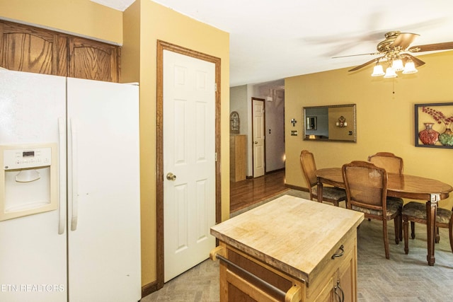 kitchen with brown cabinetry, a kitchen island, baseboards, ceiling fan, and white fridge with ice dispenser