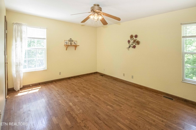 unfurnished room with plenty of natural light, a ceiling fan, wood finished floors, and visible vents