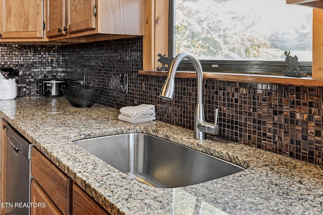 kitchen featuring stainless steel dishwasher, light stone countertops, brown cabinets, tasteful backsplash, and a sink