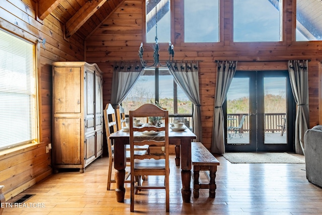 dining space featuring beam ceiling, wooden walls, high vaulted ceiling, french doors, and light wood-style flooring