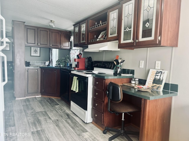 kitchen featuring electric range, built in desk, glass insert cabinets, under cabinet range hood, and light wood-style flooring
