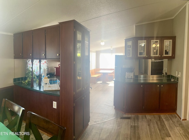 kitchen with light wood-style floors, vaulted ceiling, and glass insert cabinets
