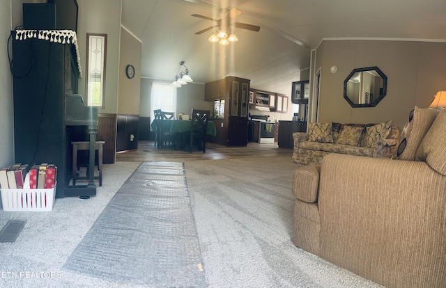 living room with a wood stove, carpet floors, a wainscoted wall, a ceiling fan, and lofted ceiling