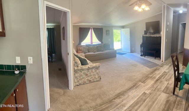 living area featuring a wood stove, a ceiling fan, wood finished floors, lofted ceiling, and ornamental molding