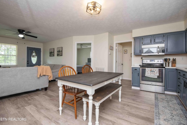 interior space with a ceiling fan, a textured ceiling, appliances with stainless steel finishes, light countertops, and light wood-style flooring