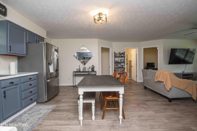 kitchen featuring a textured ceiling, stainless steel fridge, light wood-style flooring, and blue cabinetry