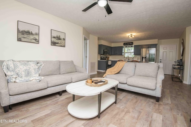 living room featuring a ceiling fan, light wood-type flooring, a textured ceiling, and visible vents