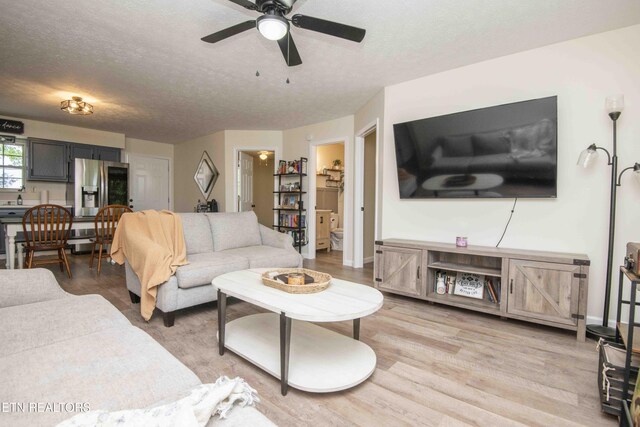 living area with baseboards, a ceiling fan, a textured ceiling, and light wood-style flooring