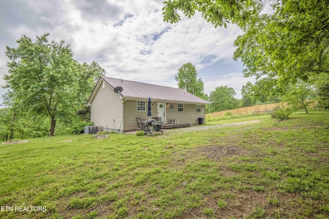 rear view of property with a yard, fence, metal roof, and central AC unit