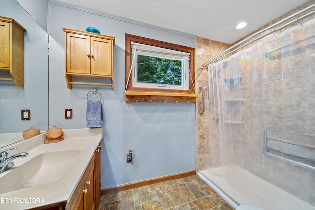 bathroom with baseboards, stone finish floor, tiled shower, and vanity