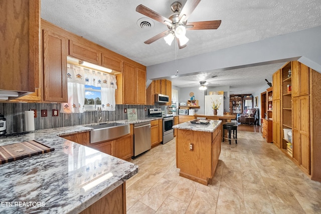 kitchen with ceiling fan, a textured ceiling, appliances with stainless steel finishes, a sink, and light stone counters