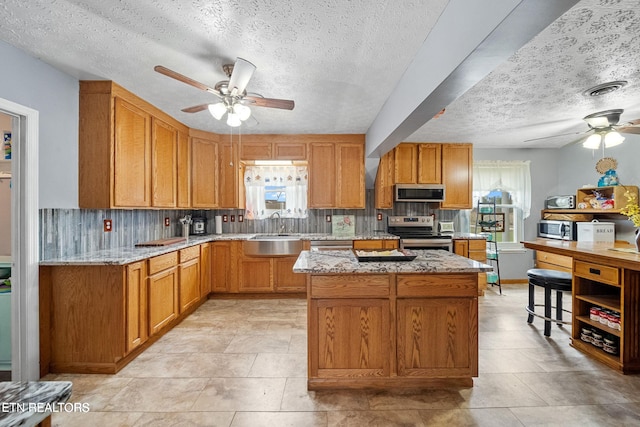 kitchen featuring ceiling fan, appliances with stainless steel finishes, a sink, a textured ceiling, and plenty of natural light