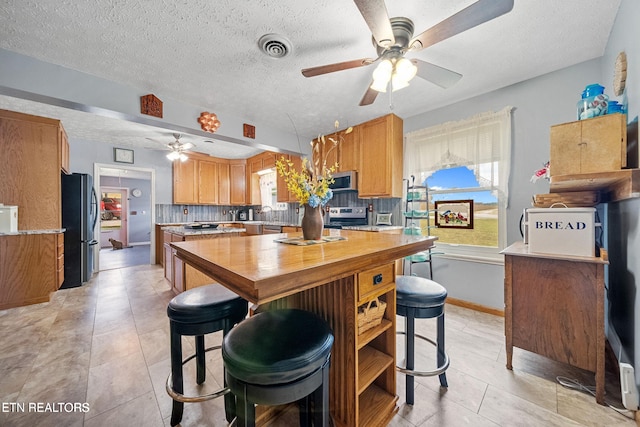 kitchen featuring stainless steel appliances, ceiling fan, decorative backsplash, and a textured ceiling