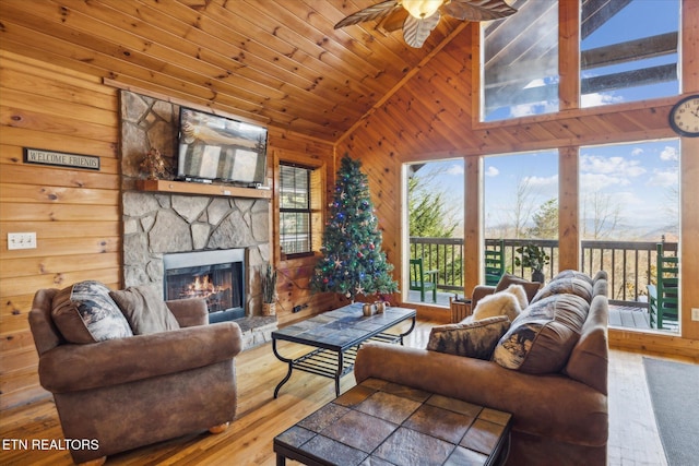living room with ceiling fan, vaulted ceiling, an outdoor stone fireplace, wooden walls, and hardwood / wood-style floors