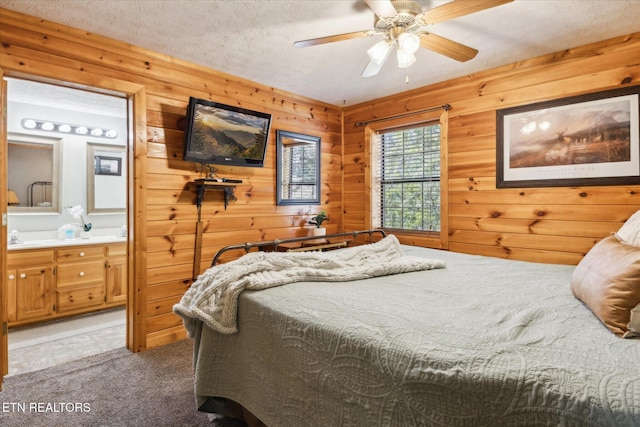 bedroom featuring ceiling fan, wooden walls, light colored carpet, a textured ceiling, and ensuite bath