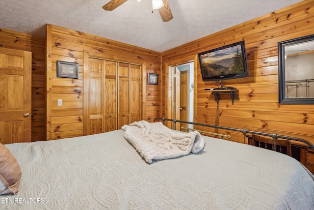 bedroom with a closet, wood walls, a textured ceiling, and ceiling fan