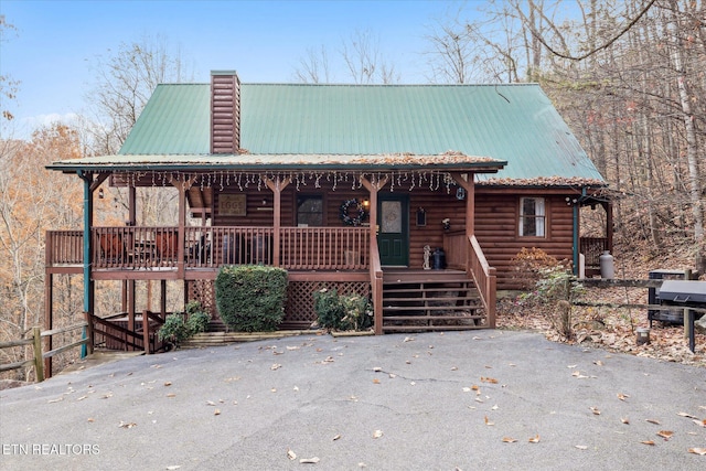 view of front of home with covered porch, a chimney, metal roof, and log veneer siding