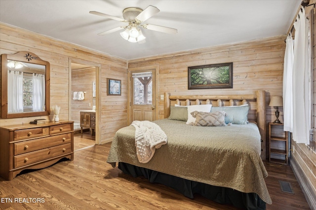 bedroom with wooden walls, visible vents, wood finished floors, and ensuite bath
