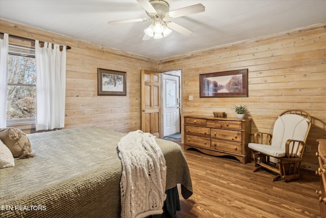 bedroom featuring a ceiling fan, wood walls, and wood finished floors