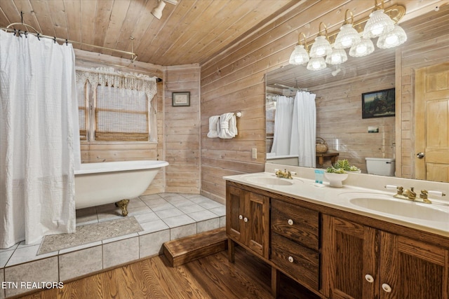 full bath with double vanity, wood walls, a sink, and a freestanding bath