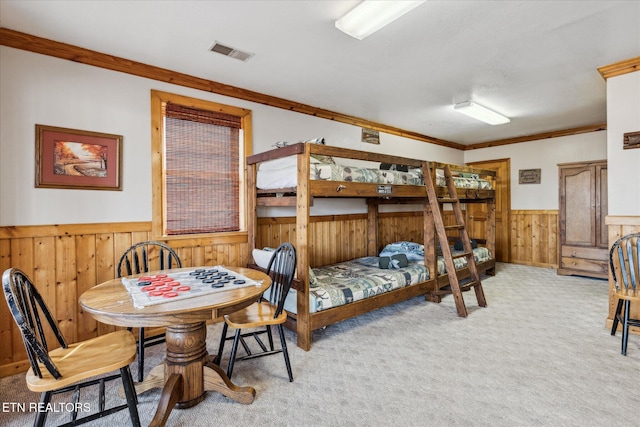 carpeted bedroom with visible vents, ornamental molding, wainscoting, and wooden walls