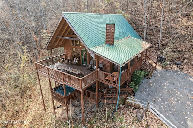 exterior space featuring a wooden deck, faux log siding, metal roof, a wooded view, and stairway
