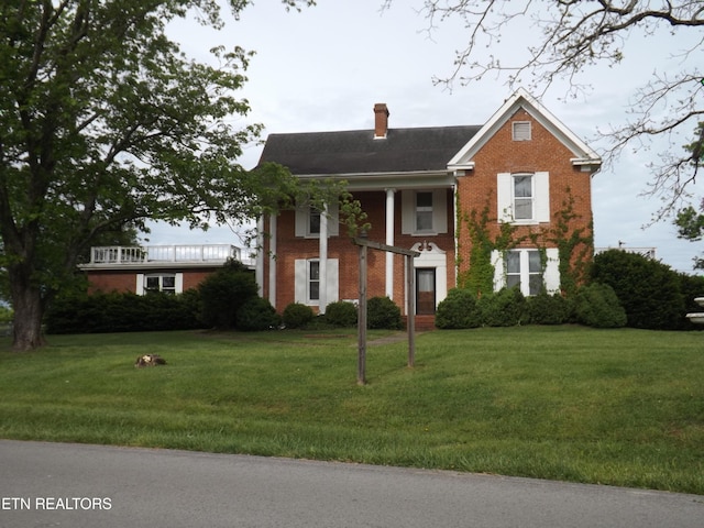 greek revival house with a chimney, brick siding, and a front yard