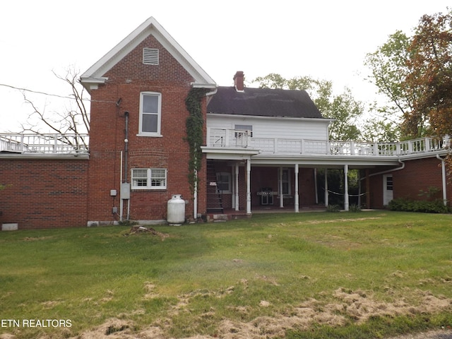 rear view of house featuring a lawn, brick siding, a wooden deck, and a chimney