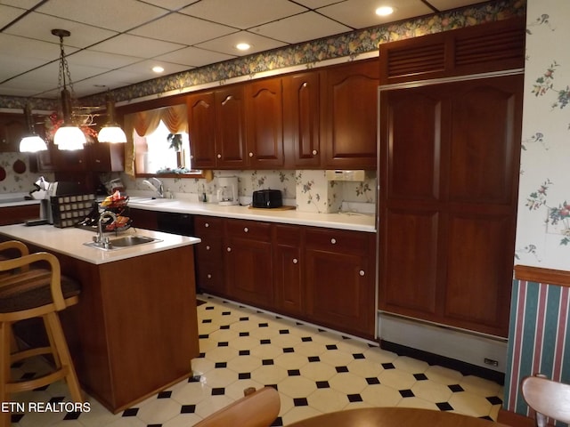 kitchen featuring a sink, light countertops, wallpapered walls, light floors, and pendant lighting