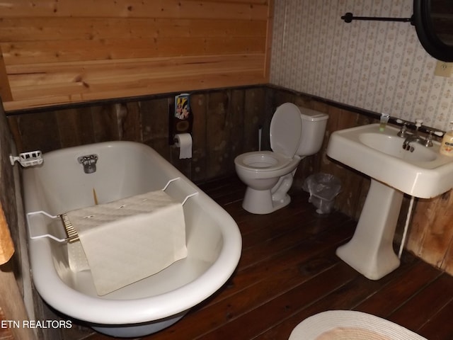 full bath featuring wallpapered walls, a wainscoted wall, hardwood / wood-style floors, toilet, and a tub
