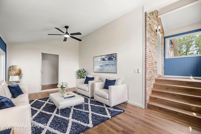 living area with a ceiling fan, lofted ceiling, wood finished floors, and stairway